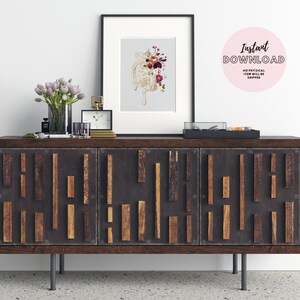 May include: A framed print of a floral anatomical heart illustration with a dark wood frame on a dark wood dresser with three drawers. The dresser has a geometric pattern of wood strips on the front. The dresser is sitting on a light gray floor. The print is on a light gray background. The flowers are in shades of pink, red, and purple. The heart is gold. The text "Instant Download" is on a pink circle.