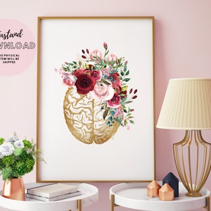 Puede incluir: Una impresión de arte digital imprimible que presenta un cerebro anatómico dorado con un arreglo floral de flores rojas, rosas y blancas. La impresión está enmarcada y se muestra en una mesa con una lámpara y otra decoración.