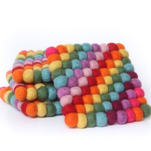 May include: Set of four colorful felt coasters with a rainbow pattern. Each coaster is made of small, round felt balls.