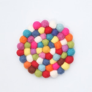 May include: A round, colorful felt ball trivet. The trivet is composed of many small, tightly packed felt balls in a variety of colors, including pink, blue, yellow, green, and orange. The trivet is designed to protect surfaces from heat.