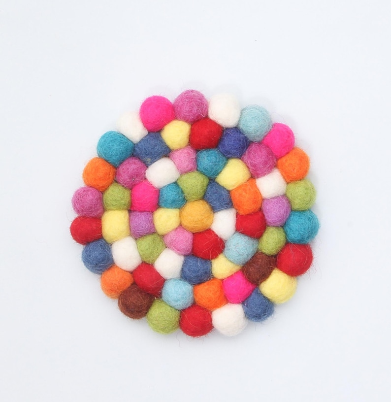 May include: A round, colorful felt ball trivet. The trivet is composed of many small, tightly packed felt balls in a variety of colors, including pink, blue, yellow, green, and orange. The trivet is designed to protect surfaces from heat.