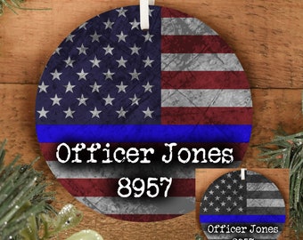 May include: A round, white, ceramic ornament with a distressed American flag design. A blue stripe with the text "Officer Jones 8957" is across the bottom.