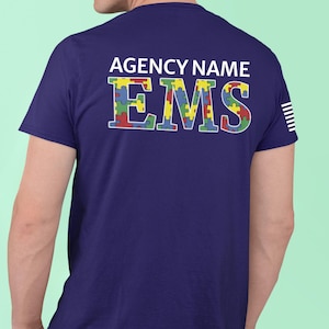 May include: Navy blue t-shirt with the text "AGENCY NAME" above the word "EMS". The letters of "EMS" are designed with a colorful puzzle piece pattern. White stripes are on the right sleeve.