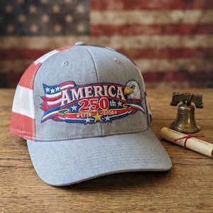 May include: Gray baseball cap with a mesh back and a curved brim. The front features an embroidered design with the word "AMERICA" above "250th" and the years "1776-2026", along with an eagle and stars.