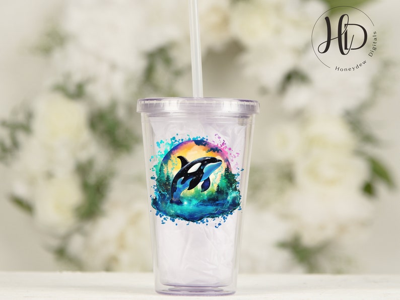 May include: A clear plastic tumbler with a colorful design featuring an orca whale jumping out of the water. The design includes a watercolor effect with shades of blue, green, and pink. The tumbler has a straw.