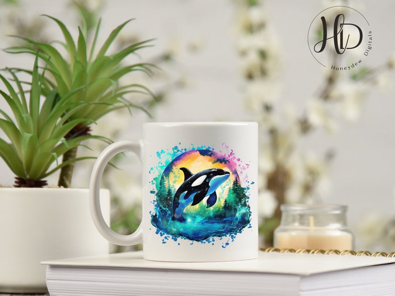 May include: White ceramic mug with a colorful watercolor design of an orca jumping out of the water. The orca is black and white, and the water is blue and green. The background is a sunset with pink and orange colors.