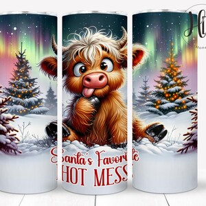 Può includere: Un bicchiere bianco con una scena natalizia che presenta una mucca pelosa marrone e bianca con la lingua rossa che sporge. La mucca è in piedi sulla neve con un albero di Natale dietro di lei. Il testo "Santa's Favorite Hot Mess" è stampato sul bicchiere.