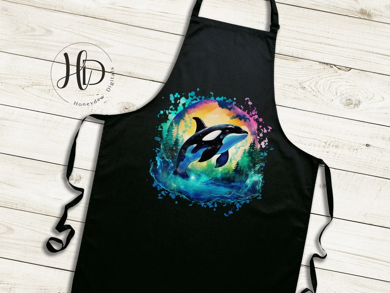 May include: Black kitchen apron with a colorful watercolor design of an orca whale jumping out of the water. The design has a rainbow color scheme with a dark blue background.