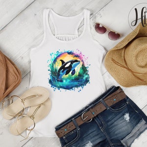 May include: White tank top with a watercolor design of an orca whale jumping out of the water. The design is surrounded by a colorful splash of paint.