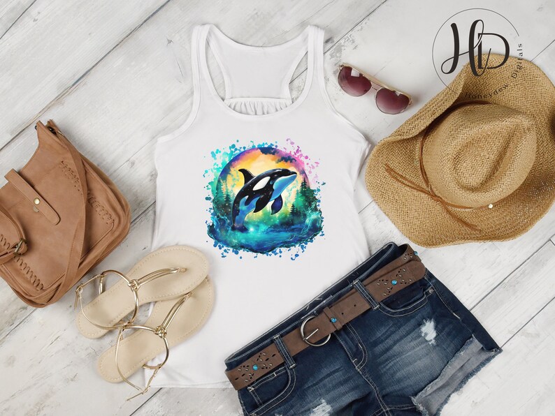 May include: White tank top with a watercolor design of an orca whale jumping out of the water. The design is surrounded by a colorful splash of paint.