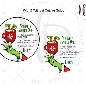 May include: A green Grinch hand holding a red mug with hot chocolate and marshmallows. The mug has a snowflake on it. The text "You're a Sweet One" is above the mug with instructions for making hot chocolate. The text "Enjoy!" is below the mug.