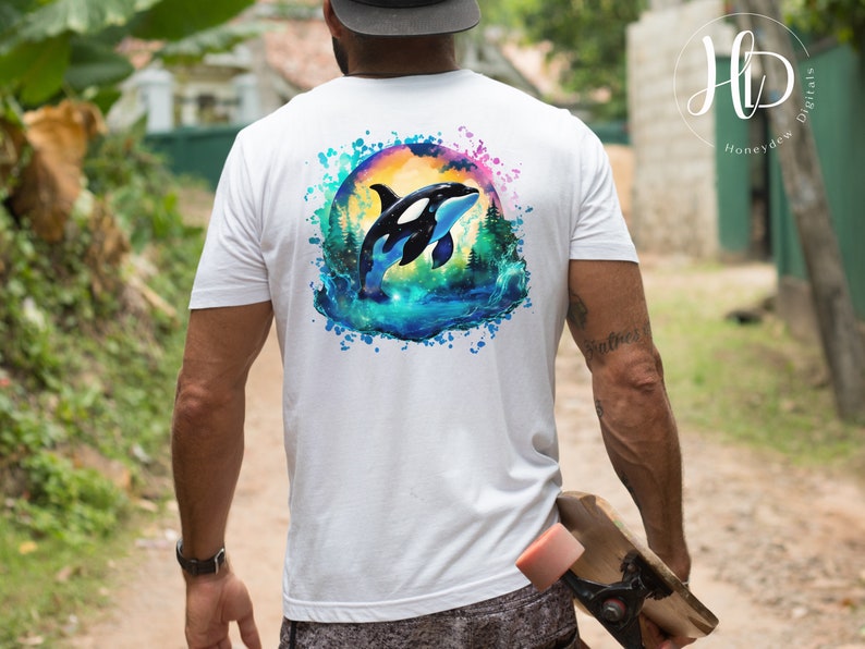 May include: White t-shirt with a watercolor design of an orca jumping out of the water. The orca is black and white with a blue and green watercolor background.
