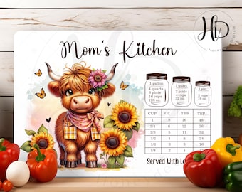 Könnte beinhalten: Ein weißes Küchenschild mit dem Text "Mom's Kitchen" in braunen Buchstaben. Eine Comic-Highland-Kuh mit einem Blumenkopfband steht in der Mitte des Schildes. Das Schild enthält auch eine Umrechnungstabelle für Tassen, Unzen, Esslöffel und Teelöffel. Das Schild ist von Sonnenblumen und Herzen umgeben.