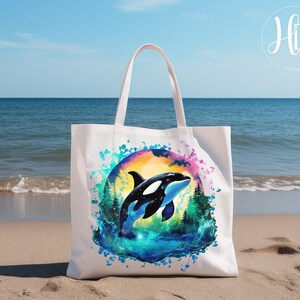 May include: White canvas tote bag with a colorful watercolor design of an orca jumping out of the water. The orca is black and white with a blue and green watercolor background.