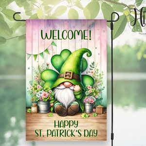 Puede incluir: Un gnomo duende verde con barba blanca y un sombrero verde con un diseño de trébol se sienta frente a una valla de madera con las palabras "¡Bienvenido!" y "Feliz Día de San Patricio".