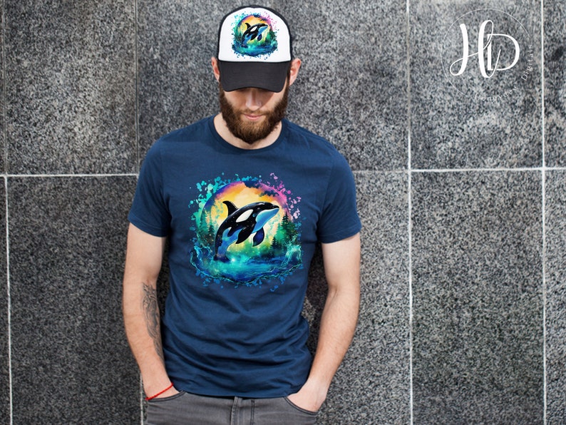 May include: A navy blue t-shirt with a watercolor design of an orca jumping out of the water. The orca is surrounded by a colorful splash of water and a sunset. The t-shirt has a white and black trucker hat with a small orca design on the front.