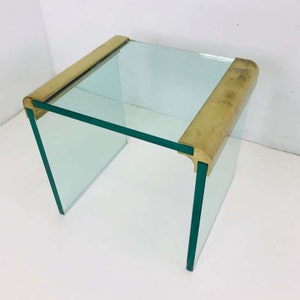 May include: A square glass side table with brass trim. The table has a clear glass top and a brass frame.