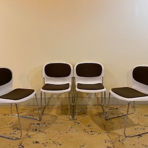 May include: Four white chairs with brown cushioned seats and chrome legs. The chairs are arranged in a row.