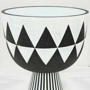 May include: A decorative white and black ceramic bowl with a geometric triangle pattern. The bowl sits on a pedestal base with vertical black and white stripes. The bowl's interior is light blue.