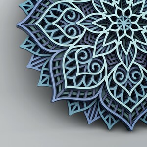 May include: A layered, three-dimensional mandala in shades of blue, teal, and gray. The intricate design features floral and geometric patterns, creating a sense of depth and complexity. The artwork is likely made of paper or wood.