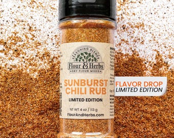 Può includere: Un barattolo di spezie trasparente con coperchio nero, etichettato "SUNBURST CHILI RUB" e "LIMITED EDITION". L'etichetta riporta anche "Flour & Herbs" e "DRY FLOUR MIXES". Il barattolo contiene una miscela di spezie marrone-rossastro, peso netto 113 g.