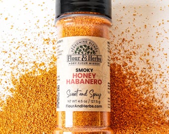 Könnte beinhalten: Eine transparente Gewürzflasche mit schwarzem Deckel, gefüllt mit orangefarbenen und braunen Gewürzen. Das Etikett lautet "Smoky Honey Habanero" und "Sweet and Spicy". Das Nettogewicht beträgt 127,5 g. Lose Gewürze umgeben die Flasche.