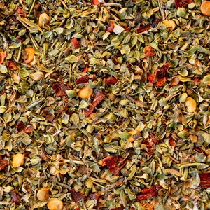 May include: A close-up of a blend of dried herbs and spices, including green herbs, red pepper flakes, and small yellow seeds.