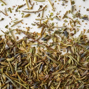 Pu&ograve; includere: Primo piano di erbe secche, tra cui rosmarino, timo e lavanda, sparse su una superficie bianca.