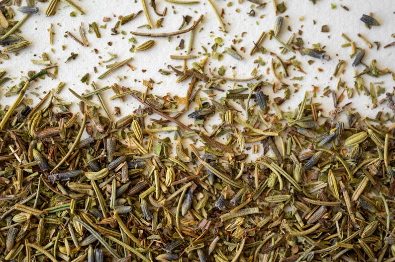 Pu&ograve; includere: Primo piano di erbe secche, tra cui rosmarino, timo e lavanda, sparse su una superficie bianca.