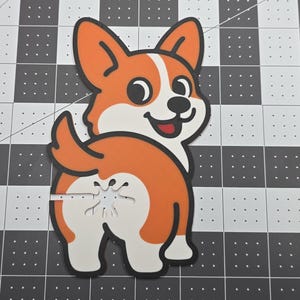 May include: A cartoon corgi dog illustration, viewed from the rear, with orange, white, and black coloring. The dog's rear end is the focal point, with a humorous design. The image is on a black and white checkered surface.