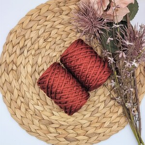 May include: Two spools of deep red cotton rope on a woven straw mat with a bouquet of pink and brown flowers.