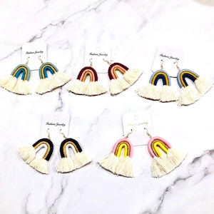 May include: A collection of rainbow-shaped earrings with gold-colored hooks and cream-colored fringe. The earrings are in various colors, including blue, red, yellow, and black. Each earring is attached to a white card with the text "Fashion Jewelry".