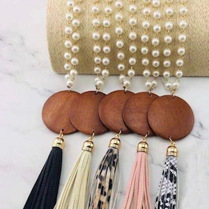 May include: A collection of long necklaces with faux pearl strands, wooden disc pendants, and colorful tassel accents. Tassels are black, cream, leopard print, pink, and black and white patterned.