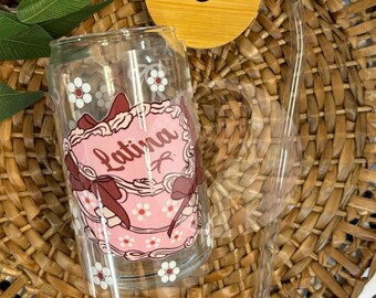May include: A clear glass tumbler with a pink and white floral design and the word "Latina" in a heart-shaped frame. The tumbler has a bamboo lid and a clear plastic straw.