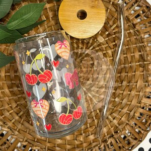 May include: A clear glass tumbler with a cherry and heart design. The tumbler has a bamboo lid and a clear glass straw.