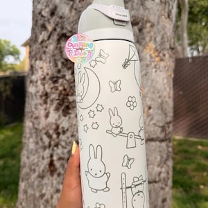 May include: A white stainless steel water bottle featuring a gray line art pattern of rabbits, butterflies, stars, and flowers. The bottle has a gray lid with a locking mechanism labeled Lift to Unlock and a circular logo sticker attached.