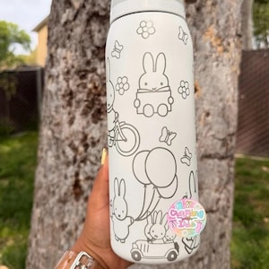 May include: A white cylindrical water bottle featuring a gray lid and a repeating line art pattern of a cartoon rabbit, flowers, butterflies, balloons, and a car. A circular sticker with the text Crafting with Die is attached to the bottle.