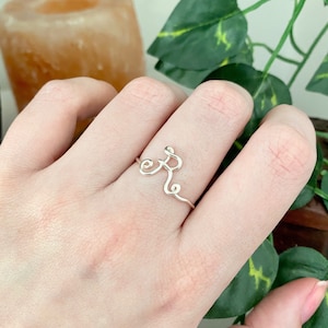 May include: A silver ring featuring the letters "RE" intertwined in a cursive style.