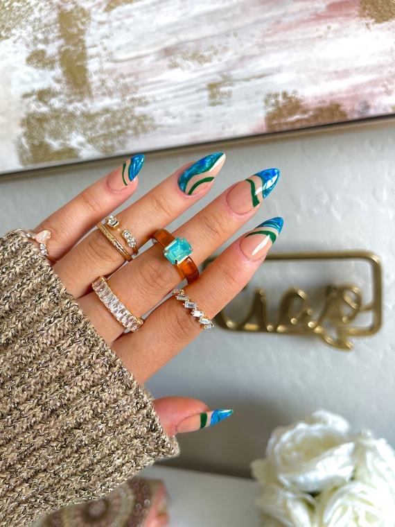 A hand with creative nail design on a green and blue water background with  waves and light sparkles Stock Photo - Alamy