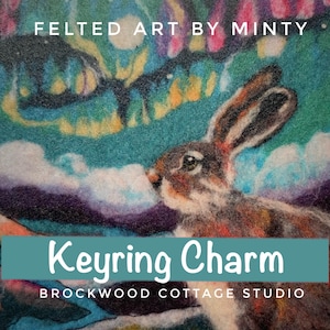 May include: A felted artwork depicting a hare with a colourful, abstract background. The text "FELTED ART BY MINTY" is at the top, and "Keyring Charm" is in a teal banner. "BROCKWOOD COTTAGE STUDIO" is at the bottom.