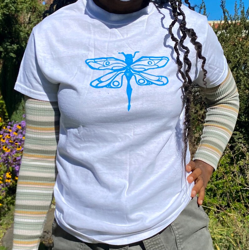 Puede incluir: Camiseta blanca con un estampado gr&aacute;fico de lib&eacute;lula azul.