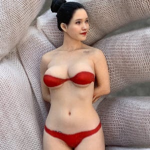 Op de afbeelding: Gedetailleerd beeldje van een vrouw met zwart haar in een knot, gekleed in een rode bikini. Het beeldje heeft een realistisch uiterlijk, met geschilderde gelaatstrekken en lichaamsdetails. De bikini bestaat uit een bandeau top en een laag uitgesneden broekje.