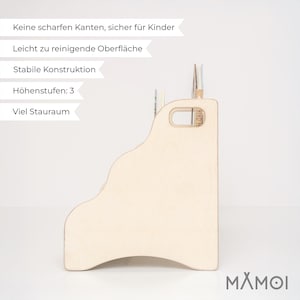 May include: A light-colored wooden bookshelf with a stepped design featuring three distinct height levels for storage. The side panel includes a cutout handle for portability. The text on the image reads: Keine scharfen Kanten, sicher f&uuml;r Kinder, Leicht zu reinigende Oberfl&auml;che, Stabile Konstruktion, H&ouml;henstufen: 3, Viel Stauraum.