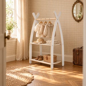 Pode incluir: Um cabideiro em forma de A, branco e de madeira clara, com uma barra superior com três camisas bege em cabides, uma prateleira central com um chapéu de palha e têxteis dobrados, e uma prateleira inferior com sapatos castanhos e um cesto de vime.