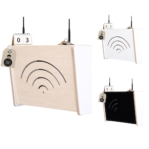 Può includere: Un router in legno con un accento bianco e un simbolo WiFi ritagliato. Il router ha un'antenna nera, un piccolo calendario che mostra "03" e un'etichetta con testo. Vengono mostrati altri due router, uno bianco e uno nero.