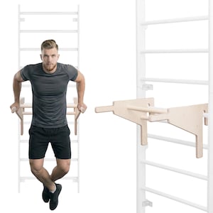 Puede incluir: Un accesorio de barra de inmersión de madera para un marco de escalada montado en la pared. El accesorio está hecho de madera de color claro y está diseñado para entrenamientos de la parte superior del cuerpo. El marco es blanco y tiene múltiples peldaños para escalar.