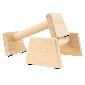 Op de afbeelding: Houten parallelle stangen voor oefeningen, met een natuurlijke houten afwerking en zwarte rubberen voetjes. De stangen zijn ontworpen voor dips, push-ups en andere lichaamsgewicht oefeningen.