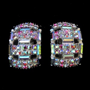 Puede incluir: Un par de pendientes de clip de tono plateado con un diseño geométrico. Los pendientes están engastados con piedras de imitación rojas, azules y verdes iridiscentes.