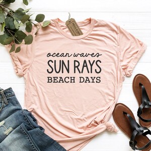 May include: A light pink t-shirt with the text "ocean waves SUN RAYS BEACH DAYS" printed in black.