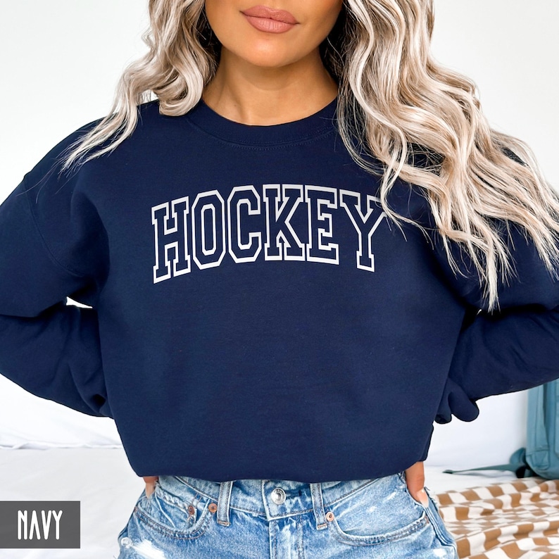 A woman wearing a navy blue crewneck sweatshirt with the word HOCKEY in white collegiate block letters.